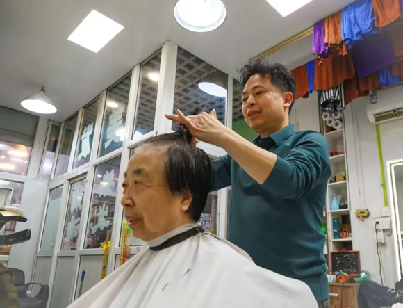 谭毓全为社区居民剪头发。唐晓洪 摄